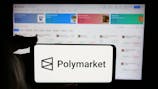 In this photo illustration, a person is holding a cellphone with the logo of crypto prediction market company Polymarket on screen in front of business webpage.