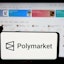 In this photo illustration, a person is holding a cellphone with the logo of crypto prediction market company Polymarket on screen in front of business webpage.