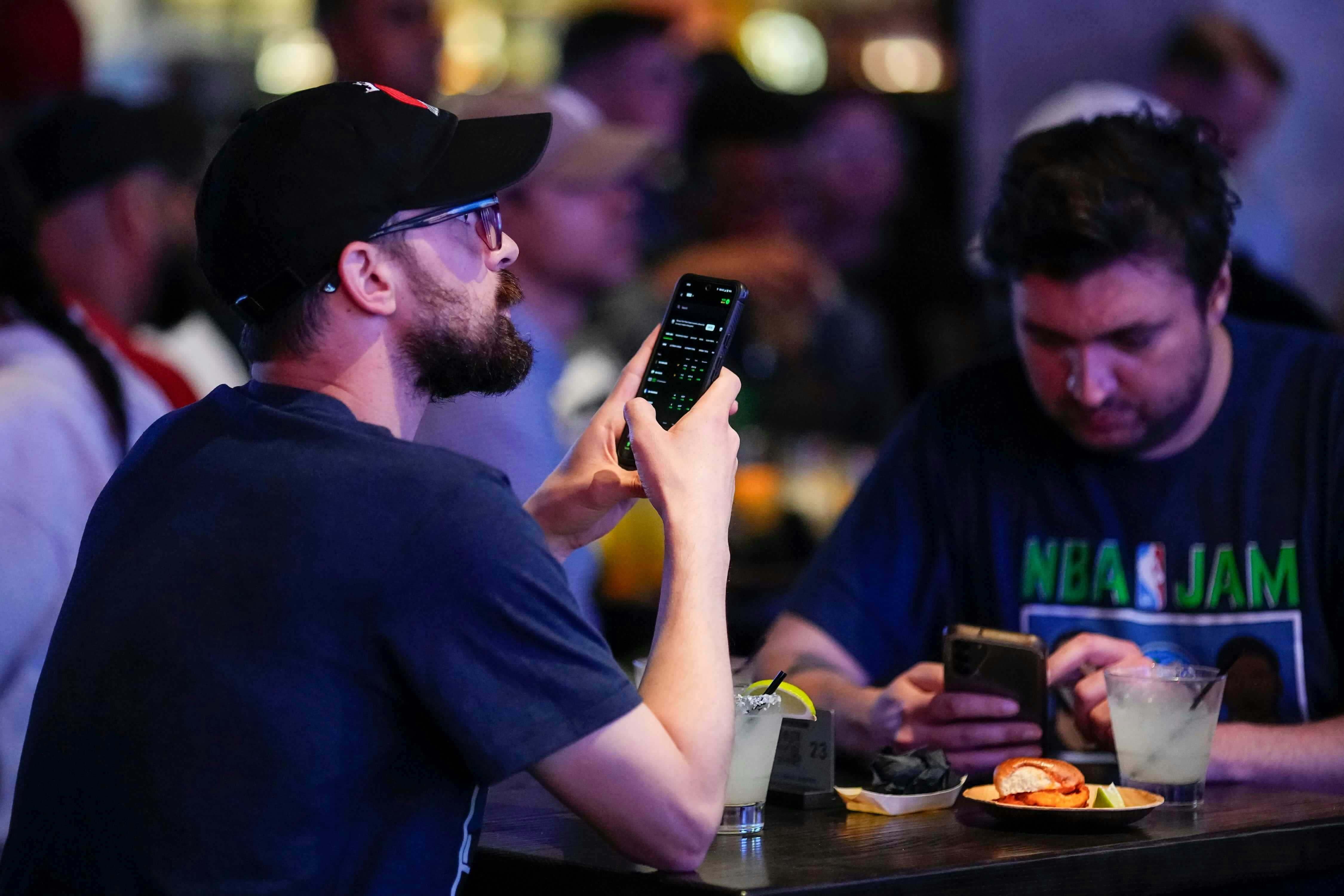 Alex Bucci, left, of Worthington and Richard Mettke of German Village use the DraftKings app during the grand opening of DraftKings Sports & Social in the Short North. Though there are no on-site betting windows, eligible customers can place bets through t