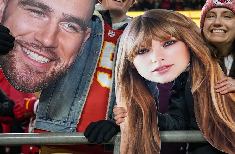 Kansas City Chiefs fans wave Taylor Swift and Travis Kelce cutouts at Arrowhead Stadium.