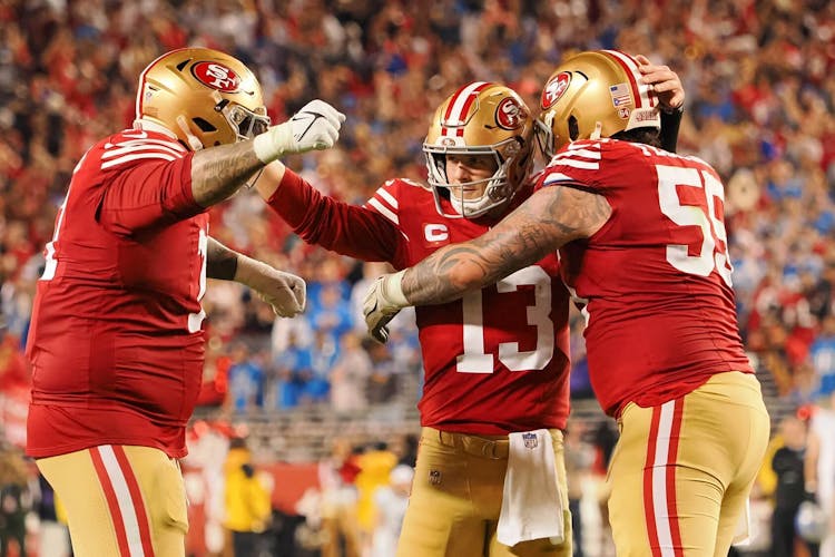 San Francisco 49ers quarterback Brock Purdy (13) celebrates with guard Jon Feliciano (55) and offensive tackle Trent Williams (71) after a play against the Detroit Lions during the second half of the NFC Championship football game at Levi's Stadium.
