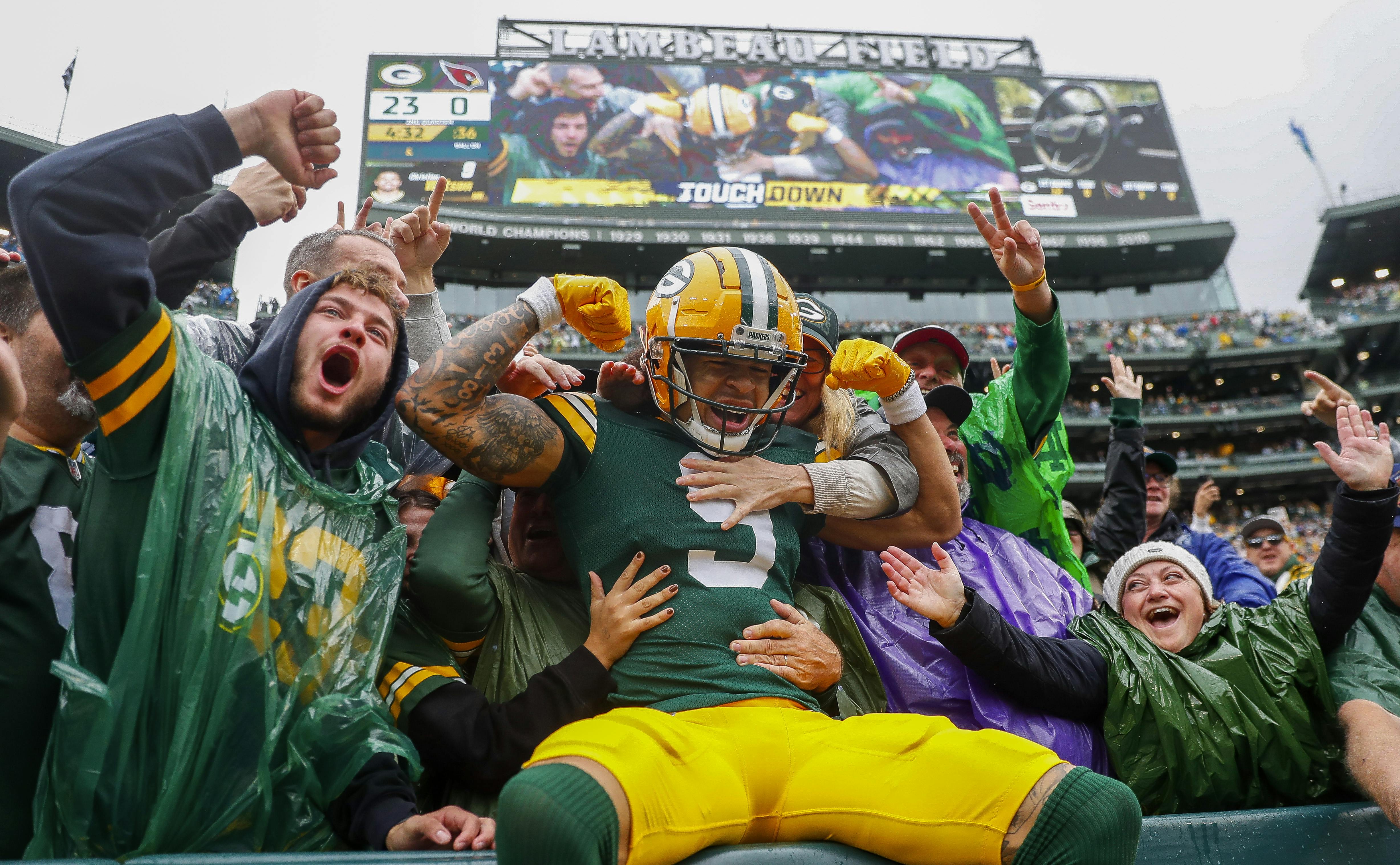 Green Bay Packers wide receiver Christian Watson (9) flexes as he does the “Lambeau Leap” with Packers fans after scoring a touchdown against the Arizona Cardinals at Lambeau Field. Mandatory Credit: Tork Mason/USA TODAY NETWORK-via Imagn Images